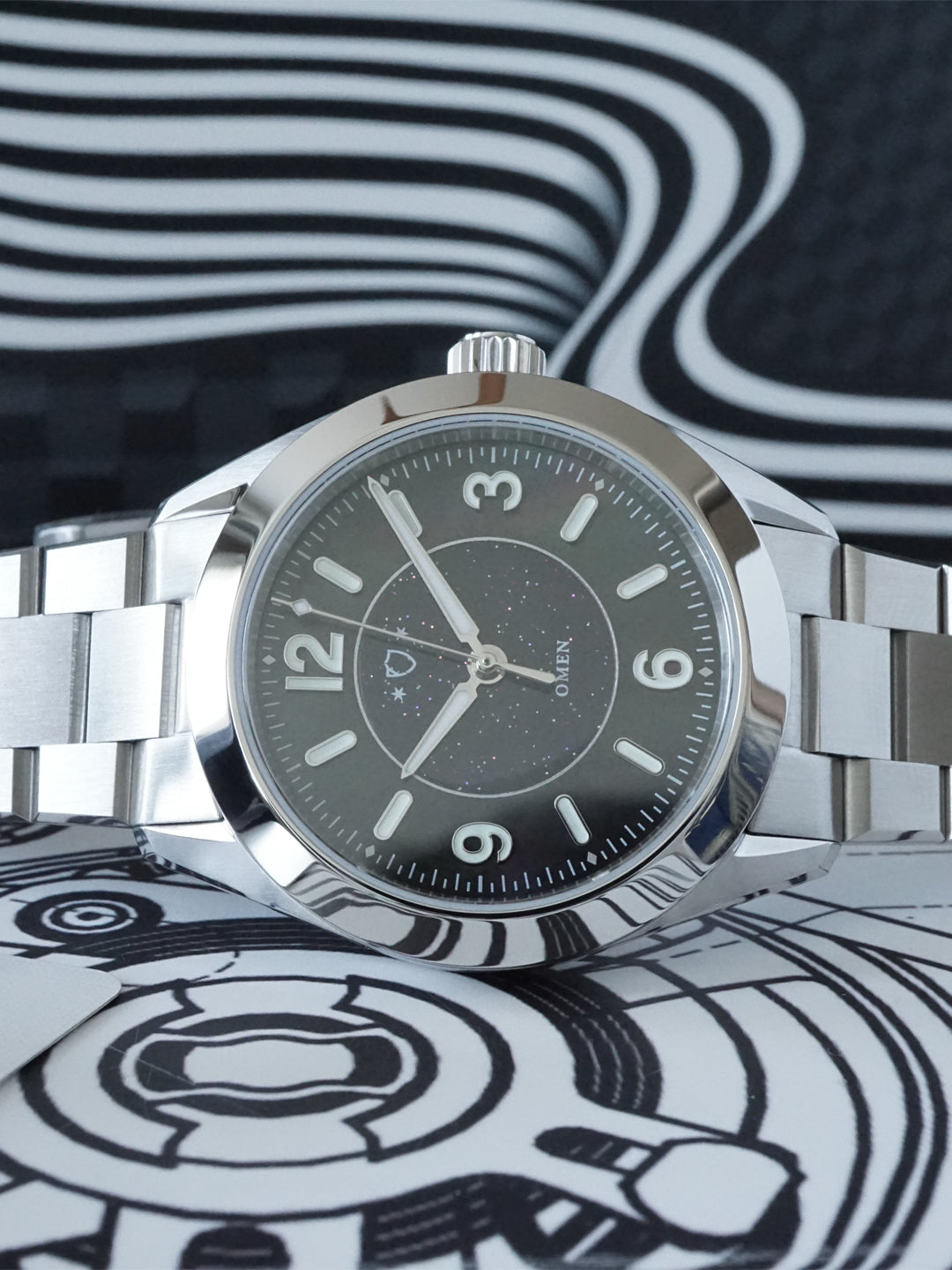 Silver watch with a black face on a black and white patterned background