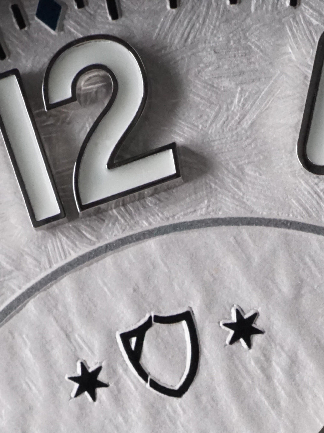 Close-up of a metallic clock face with the number 12 and decorative elements.