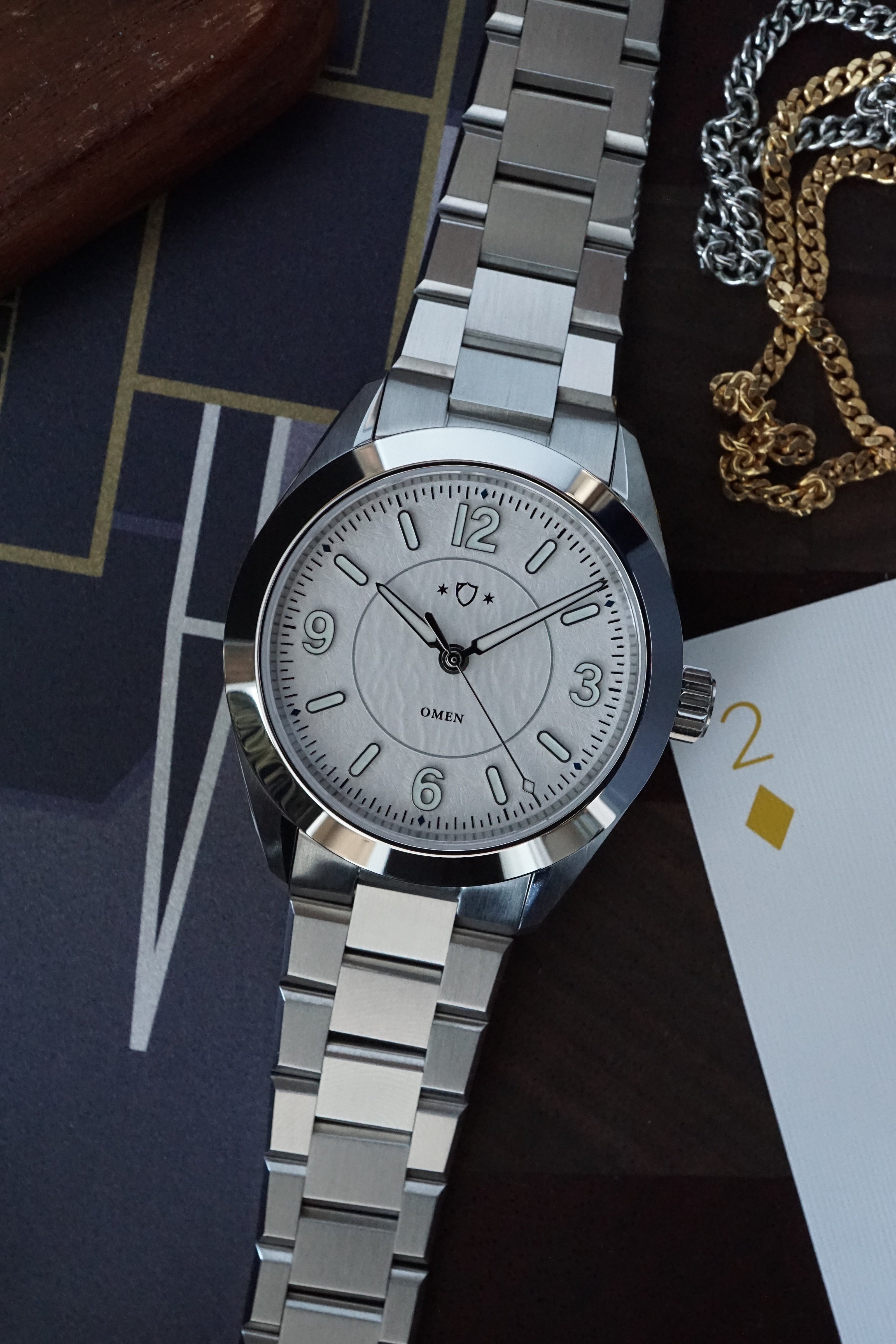 White watch with a detailed face on a dark surface with cards and chains.